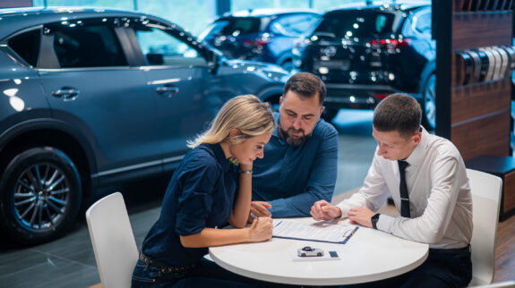 Happy caucasian couple signs a contract for the purchase of a car salon. Automotive CRM Software